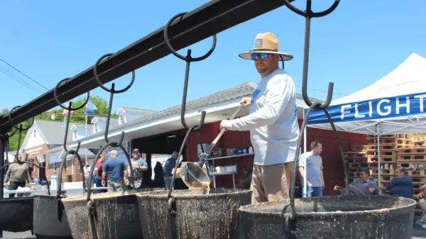 Troy Miller stirs the bean soup in one of the massive cast iron kettles hanging over a fire pit at the Friendship Fire Co. block party in Englewood.